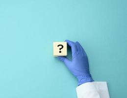 wooden cube with a question mark in the doctor's hand on a blue background. The concept of finding an answer to questions photo