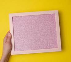 female hand holds empty pink frame on yellow background. Place for inscription photo