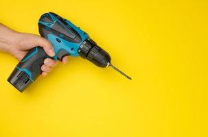 female hand holds a cordless drill on a yellow background. Tool for work photo