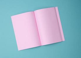 open notebook with blank pink sheets on blue background, top view photo