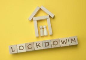 two wooden figures of a family inside a decorative house and an inscription on wooden blocks lockdown, yellow background photo