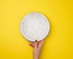 female hand holding an empty round plate on a yellow background, top view photo