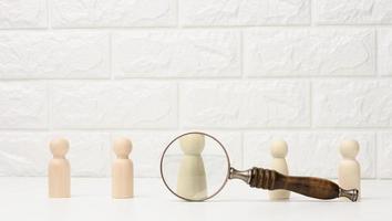 wooden figures of men stand on a white background and a magnifying glass. Recruitment concept, search for talented and capable employees, career growth photo