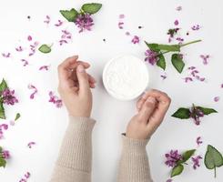 female hands and a jar with thick cream and pink flowers with green leaves photo