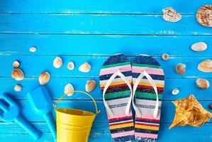 pair of female beach slippers, a yellow baby bucket and scattered seashells photo