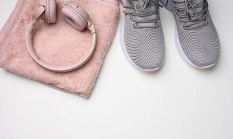 pair of gray textile sneakers, wireless headphones and a textile pink towel on a white background. Set for sports, running photo