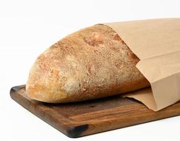 whole baked oval bread made from white wheat flour in a paper bag on a wooden board photo