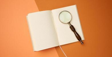 open notebook with blank sheets and wooden magnifier on orange background, top view photo
