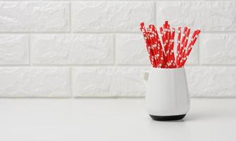 ceramic cup with red paper cocktail tubes on white table, white brickwork background photo