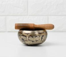 Tibetan singing copper bowl with a wooden clapper on a white wooden table, objects for meditation and alternative medicine photo