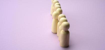 wooden men stand in a row, one figurine sticking out in front. The concept of exclusivity photo