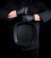 Chef in black uniform and black latex gloves holding an empty square grill pan photo