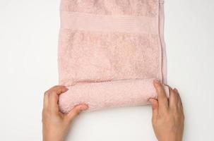 female hand holds a pink terry towel on a white table, top view photo