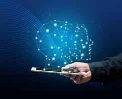 a male hand holds a tablet and a holographic drawing of a robot head. The concept of learning artificial intelligence to improve search engines, application performance and satisfaction of needs photo