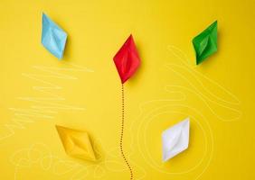 Paper boats with different trajectories on a yellow background. The concept of extraordinary thinking photo