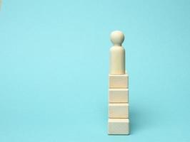 a wooden figurine of a man stands on a ladder of blocks at the very top. The concept of achieving the set goals in business photo