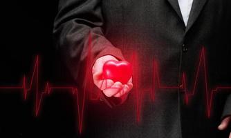 businessman holding a red heart on a black background, in front of him is a cardiogram. Office workers cardiovascular disease concept