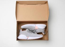 pair of gray textile sneakers in an open brown paper box on a white table photo