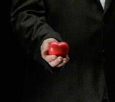 man's hand holds a red heart on a dark background photo