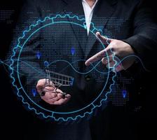 Man in a black suit holds a miniature cart against the background of a holographic graph with increasing indicators. Growth in business sales photo