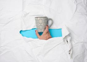 female hand holding a ceramic mug on a background of white torn paper photo