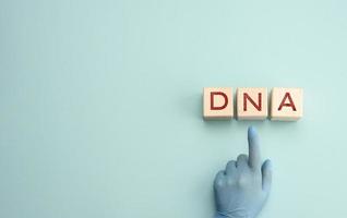 abbreviation DNA on wooden square blocks. A hand in a blue glove points to an object photo