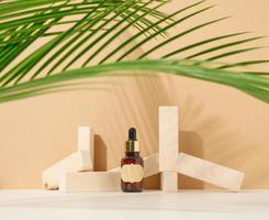 brown glass bottle with a pipette and a brown label stands on a brown background. Container for cosmetics, serum and oil. Palm leaf shadow photo