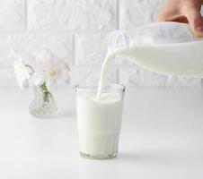 process of pouring fresh milk from a plastic bottle into a glass cup, white table photo