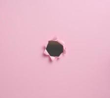 hole with torn edges in pink paper, full frame photo
