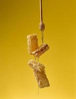 pouring transparent sweet honey from a wooden stick on a wax honeycomb. Yellow background. Food levitates photo