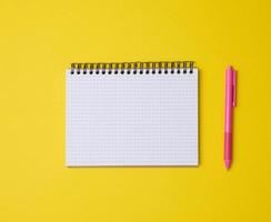 open notebook in a cage with white blank sheet and on a yellow background, top view photo