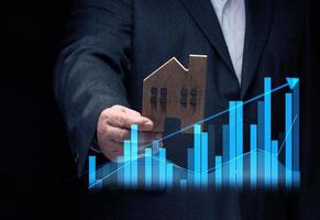 hand holds a wooden model of a house on a dark background. Real estate sale and purchase concept, rise in property prices photo