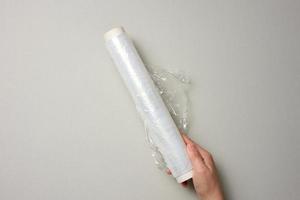 two female hands hold a roll of transparent cling film for packaging products, gray background photo