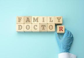 de madera bloques con el inscripción familia médico y un del doctor mano en un azul látex guante. foto