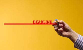 red line with the inscription deadline and a female hand with a marker on a yellow background. The concept of setting time limits photo