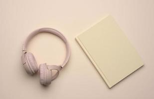 beige inalámbrico auriculares y un cerrado bloc en un beige antecedentes foto