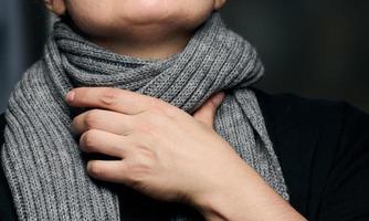 a gray scarf is wrapped around the neck, and a hand is holding the throat. Cold and sore throat photo