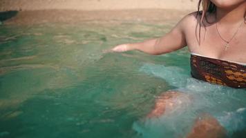 un asiático mujer es nadando en el playa con azul mar agua cuando ella se sienta en el playa arena video