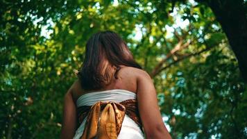 un asiático mujer en pie en el sombra de un árbol en el medio de un tropical selva en un isla solo video