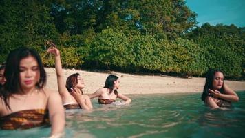 ein Gruppe von asiatisch Frauen im braun Kleider ist genießen das Blau Meer Wasser durch Tanzen mit ihr freunde auf das Strand auf ein Insel video