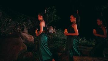 a group of Asian women walking together while holding bamboo masks in both hands and wearing green clothes in the middle of the forest video