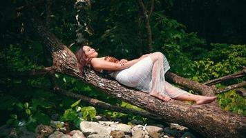 ett asiatisk kvinna är sovande på en träd trunk full av grön löv medan njuter de lugnande öns atmosfär video
