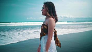 An Asian woman in a white dress walking alone on the beach with a sad expression and the sea waves behind her video