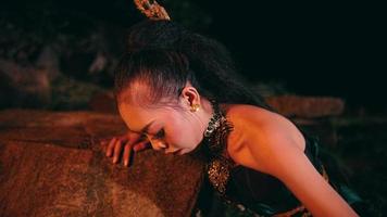 un asiático mujer llantos cuando ella es acerca de a sentar en un rock impotente y se inclina en contra un rock en el medio de un bosque video