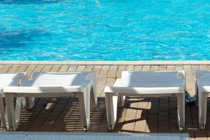 White sun loungers by the pool with blue bright water, copy space photo