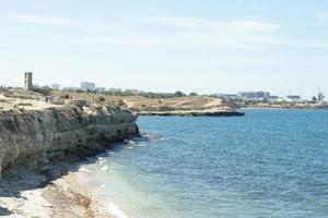 Rocky seashore with tourists. Coastal town in summer. Blue sky and water photo