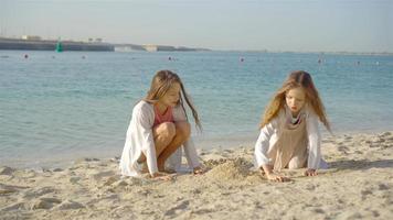 två liten Lycklig flickor ha en massa av roligt på tropisk strand spelar tillsammans video