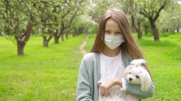 niña pequeña con perro con máscara médica protectora para prevenir virus al aire libre en el parque video