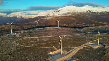 molinos de viento en las colinas durante la puesta de sol. energía renovable, energía verde. montañas en el fondo con nieve. energía eólica y respetuoso con el medio ambiente. Futuro sostenible. acabar con los combustibles fósiles. video