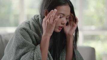 beeldmateriaal van ongelukkig verdrietig Aziatisch vrouw in een mantel lijden van koorts en griep met hoofdpijn aan het liegen Aan bankstel in de leven kamer. Gezondheid zorg en medisch concepten. video